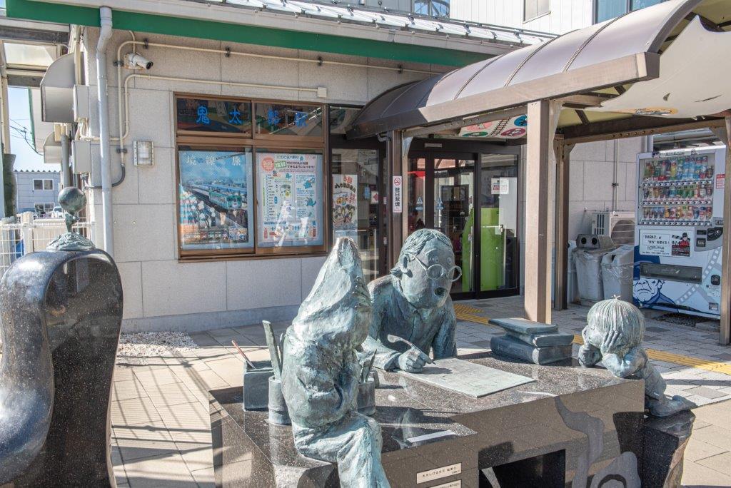 境港車站外有正在作畫的作者水木茂老師，和旁邊專心看著的鬼太郎、鼠男與眼球老街銅像。