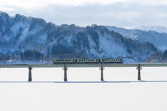 花輪線上的火車穿過白雪覆蓋的稻田，背景為岩手山。(Image credit: JR East / Go Takahashi)